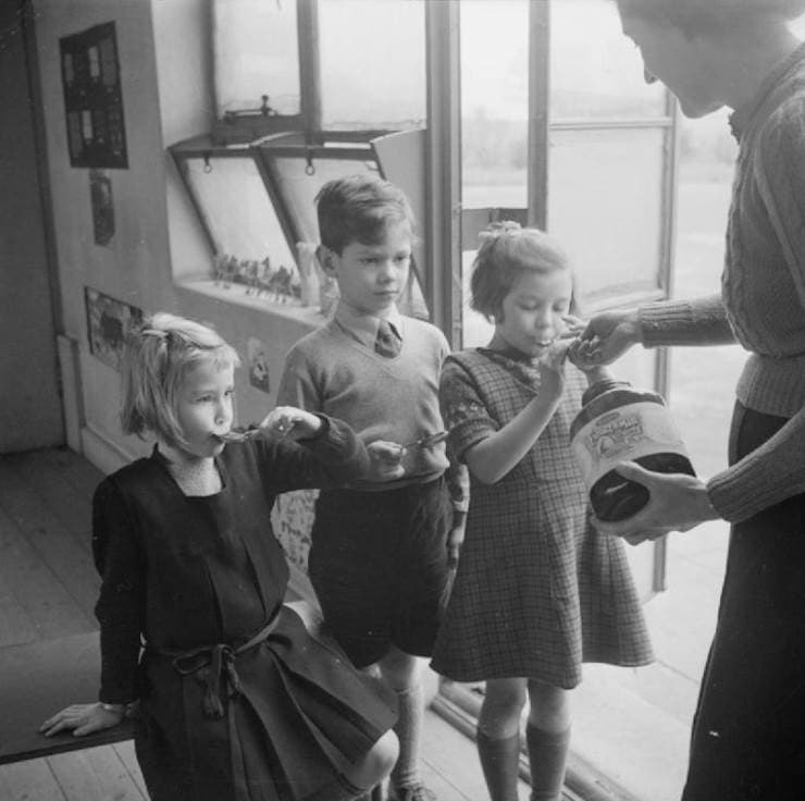 Pupils receive spoonfuls of Extract of Malt and Cod Liver Oil from their teacher at Fen Ditton Junior School, Cambridgeshire, 1944